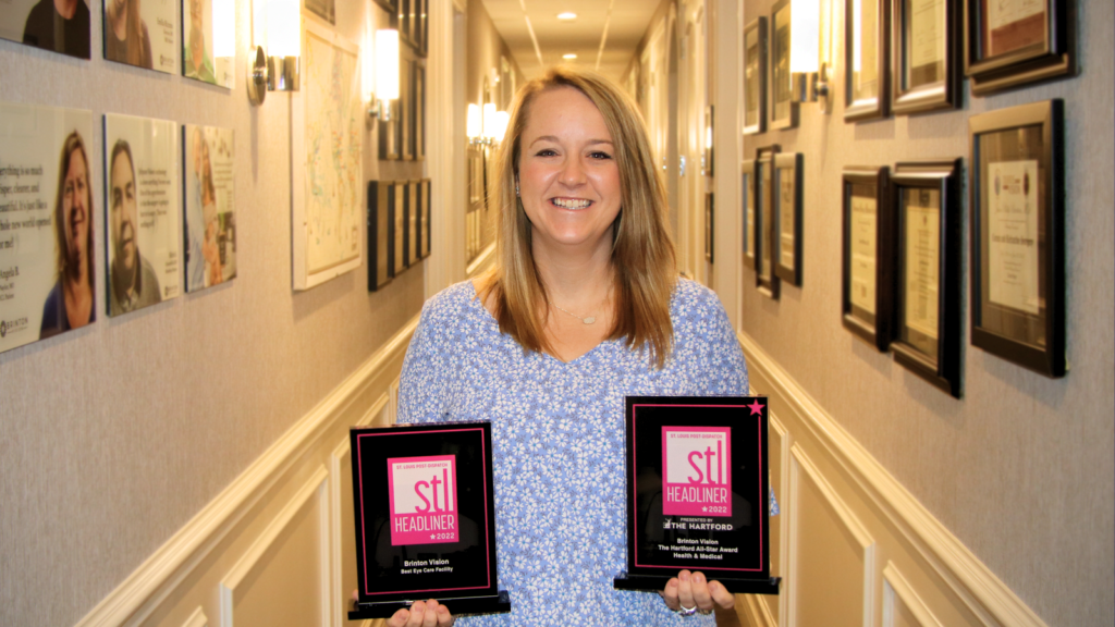 STL Headliner award; woman holding the STL awards, one in each hand. She is in a hallway with photos, degrees, and awards lining the walls