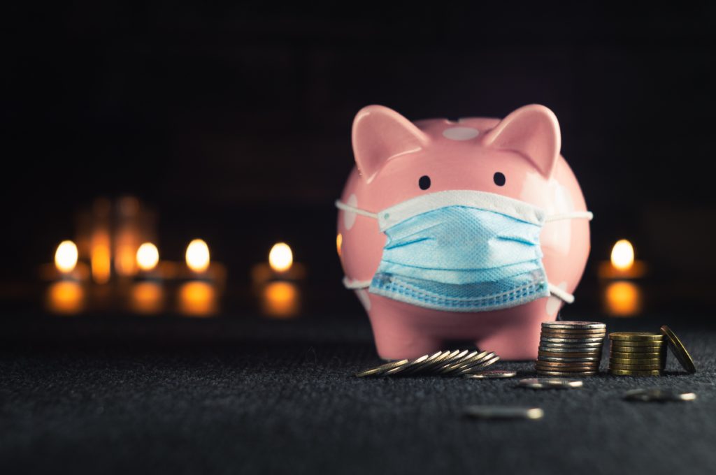 Can I Use My HSA or FSA for LASIK?; piggy bank wearing a medical mask to the right, with stacks of coins beside it. Behind it are lit candles in the dark